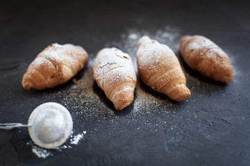 four croissants with a fruit filling, sprinkled with powdered sugar on a dark gray background