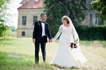 Romantic lovely newly married couple posing in the park by the medieval castle on their wedding day.