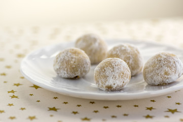 Christmas cookies, tasty balls with hazelnut inside and icing sugar, white plate and tablecloth with golden stars