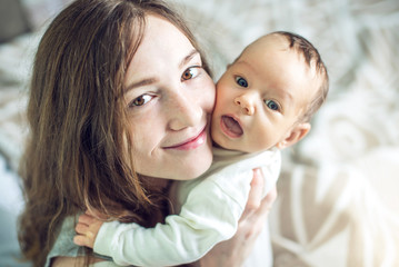 Happy caring mother holding baby boy in the bedroom. Concept of the tenderness of motherhood and family values