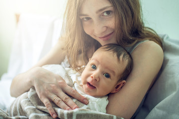Happy caring mother holding baby boy in the bedroom. Concept of the tenderness of motherhood and family values