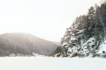 winter landscape: the valley of the frozen river between the rocky coasts, illuminated by the pinkish sun light that broke through the clouds