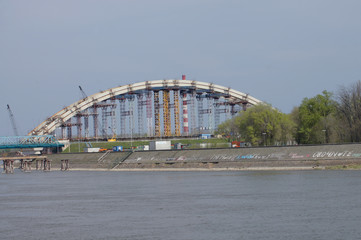 The arch of the bridge under construction. Carriers ensure arch stability. Facing architectural solutions of the old and the new bridge. The inscriptions are found on rocky shore of the river.  