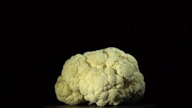 Cauliflower rotates on a black background, view shot vegetable with seamless looping.