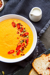 Pumpkin soup in white plate with spice on dark background