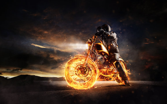 Fototapeta Dark motorbiker staying on burning motorcycle in sunset light