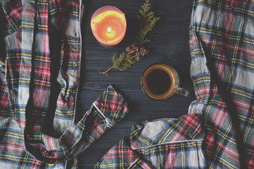 A cup of coffee, pajamas and lighted candle on the wooden background. Cozy home style. Atmospheric picture.