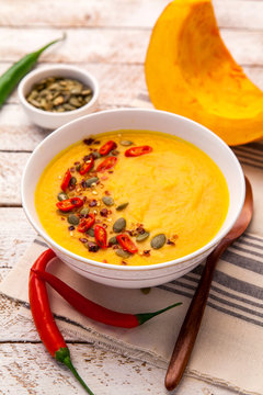 Pumpkin soup with cream and seasoning in white bowl on rustic wo
