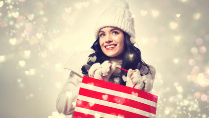 Happy young woman holding a shopping bag on shiny hearts background