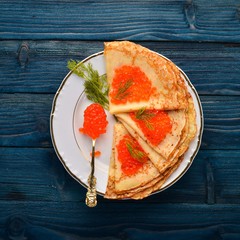 Pancakes with red caviar on a plate. On a wooden background. Top view. Free space for text.