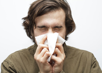 Ill person with symptoms of virus flu or allergy,  blows his nose. Healthcare medical and pharmaceutical concept. Isolated on abstract white background close up. Selective focus and shallow DOF