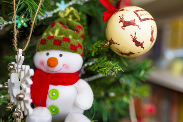 Cute smiling felt fabric snowman decoration on a Christmas tree with a reindeer bauble in the background