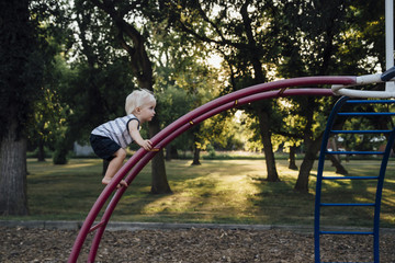 Side view of baby boy climbing monkey bars at playground