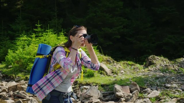 A female photographer takes pictures of nature. In a picturesque place in the background of a forest near a mountain river. Active lifestyle