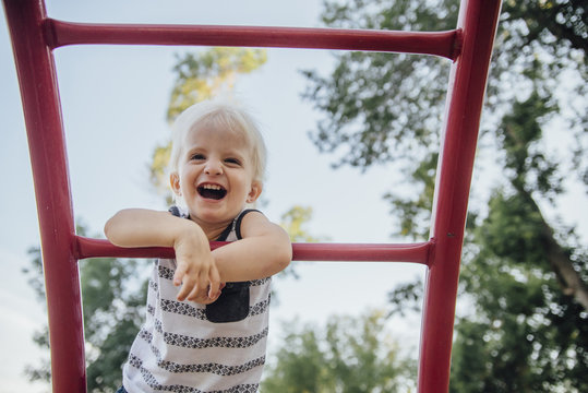 Low angle view of cheerful baby boy laughing while standing on monkey bars at park