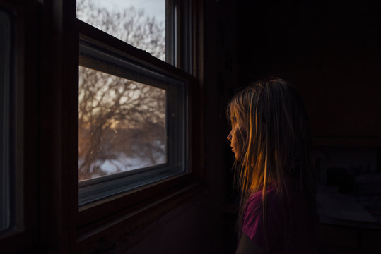Side view of girl sitting by window in darkroom