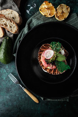 Restaurant serving tartar with salmon and avocado in the shell and a glass of white wine on a dark green concrete background