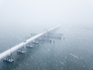 Drone shot of blizzard over bridge across river.