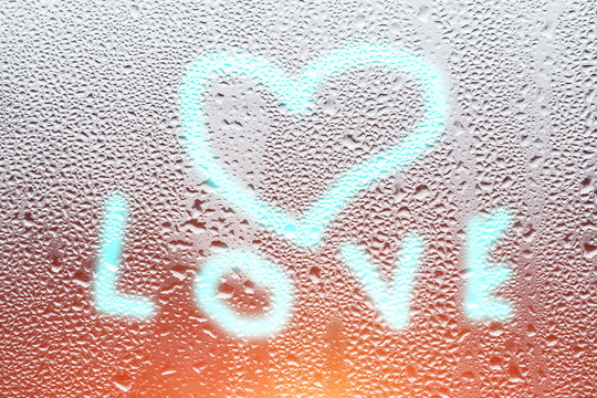 background texture wet misted glass window covered with drops of water dew with a painted love symbol of a heart with a bright color