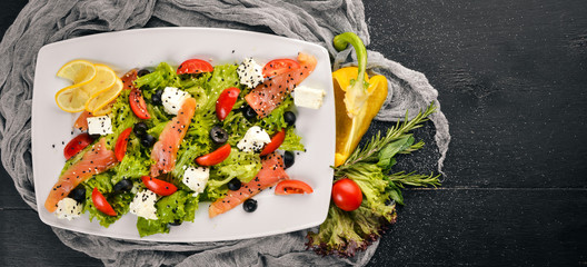 Salmon salad, feta cheese, salad leaves and fresh vegetables on the plate. On a wooden background. Top view. Free space for text.
