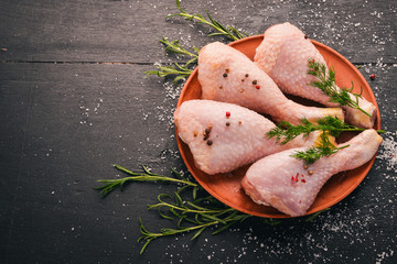 Raw chicken legs with rosemary and spices on a black wooden background. Top view. Free space for text.