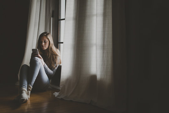 Full length of teenage girl using smart phone while sitting by window at home