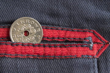 Denmark coin denomination is one krone (crown) in the pocket of worn blue denim jeans with red stripe