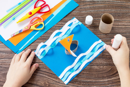 Child sticks paper boat parts, congratulations concept of Father's Day. Glue, scissors and paper on a wooden table. Children's art project craft for kids. Craft for children.