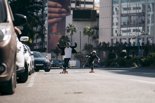 Male Friends Skateboarding On Road In City During Sunny Day