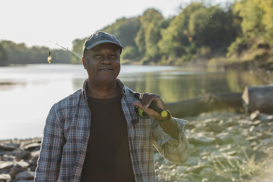 Portrait of smiling man holding fishing rod while standing at lakeshore