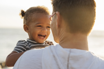 Rear view of father carrying happy daughter while standing at beach during sunset