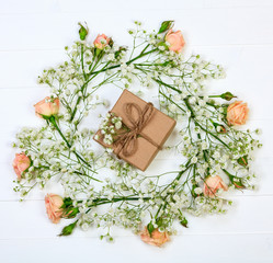 Flowers with a gift box on white wooden table, flat lay style