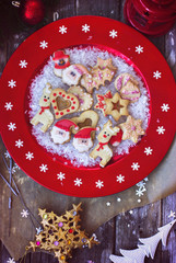 Royal icing decorated christmas cookies on in red festive plate on wooden background; with copy space