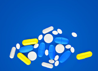 Assorted pharmaceutical medicine pills, tablets and capsules on blue background