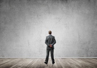 Businessman with hands behind his back and looking at blank concrete wall