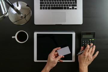 Internet shopping concept.Top view of hands working with calculator and laptop and credit card and tablet computer on dark wooden table background