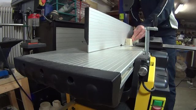 young woodworker planing wood strait on the jointer in his home business workshop.