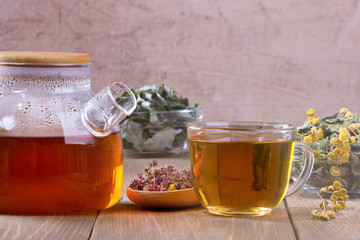 Glass teapot and cup with herbal tea on  wooden table.