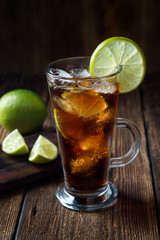 Rum and cola Cuba Libre drink with brown rum, cola, ice and lime on rustic wooden table