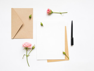 Letter and eco paper envelope on white background. Invitation cards, or love letter with pink roses. Holiday concept, top view, flat lay