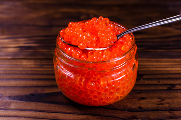 Red caviar in a spoon above the glass jar