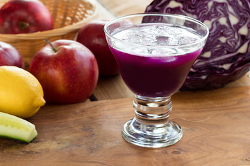 Purple cabbage juice in a glass, with cabbage and apples in the background