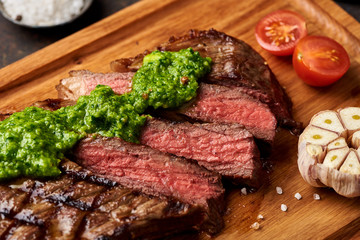 Grilled Black Angus Steak with tomatoes, garlic with chimichurri sauce on meat cutting board.