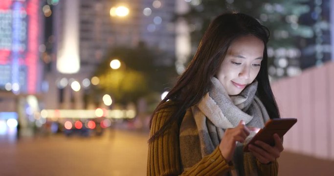 Woman looking at smart phone in the city at night