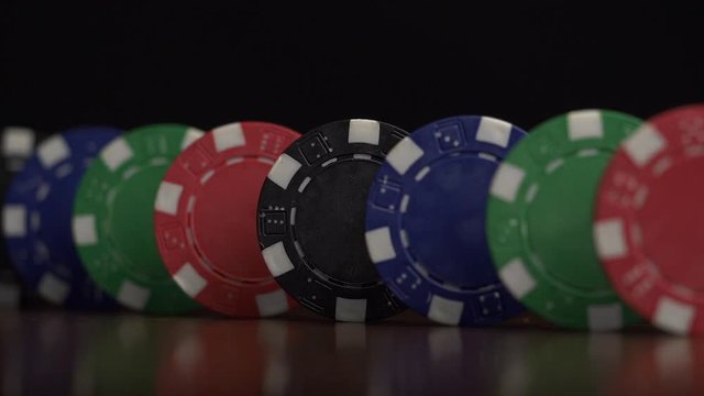 Poker chips stand in a row on a black background, a Domino effect. Playing poker chips are on the table, a symbol of casino