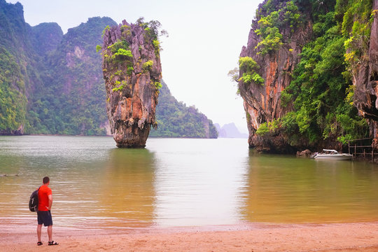 Tourist, a man, vatches James Bond Island, Phang Nga, Thailand, Asia. Monsoon, rainy wether landscape..