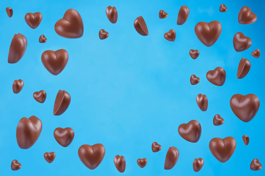 Heart shaped chocolate candies falling on blue background. Valentine's Day, confectionery, chocolate texture with copy space