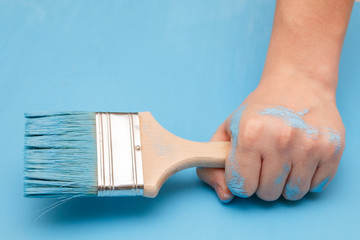 Male hand covered in paint, holding a paint brush on a wooden background surface, painted with blue paint
