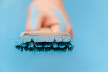 Male hand covered in paint, holding a paint brush on a wooden background surface, painted with blue paint