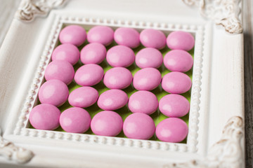 Vintage white frame with pink circle candy arranged in the center.